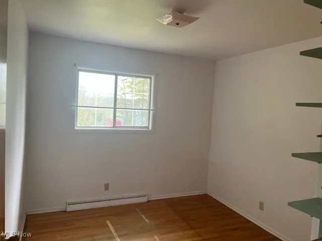 Unfurnished room with wood finished floors and a baseboard radiator