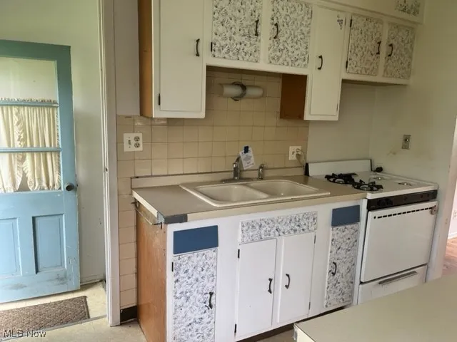 Kitchen featuring white range with gas cooktop, decorative backsplash, light countertops, and white cabinets