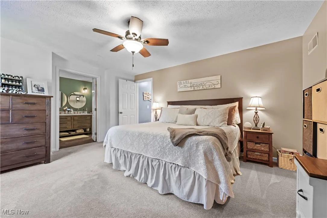 Bedroom featuring light carpet, a textured ceiling, ensuite bath, and ceiling fan