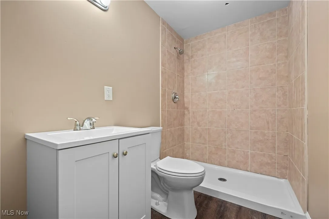 Full bathroom featuring a tile shower, vanity, and wood finished floors