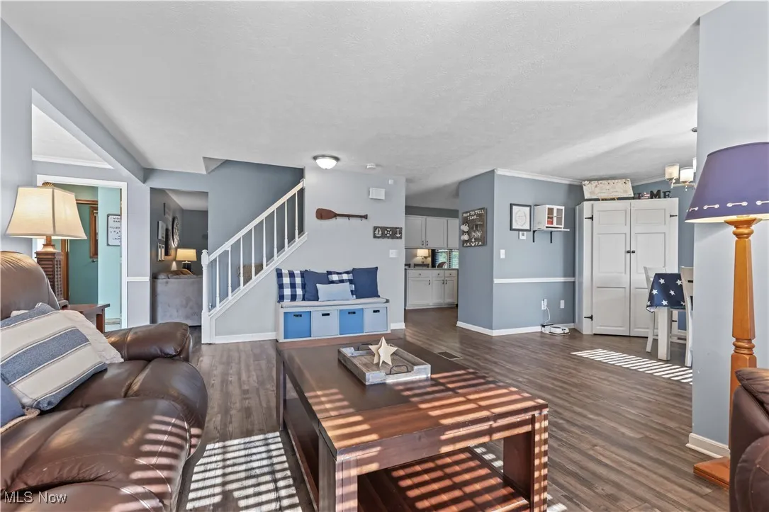 Living area with stairs, dark wood-type flooring, crown molding, and a textured ceiling