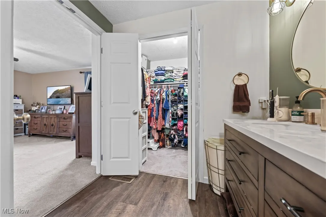 Bathroom with vanity, a textured ceiling, wood finished floors, and a walk in closet