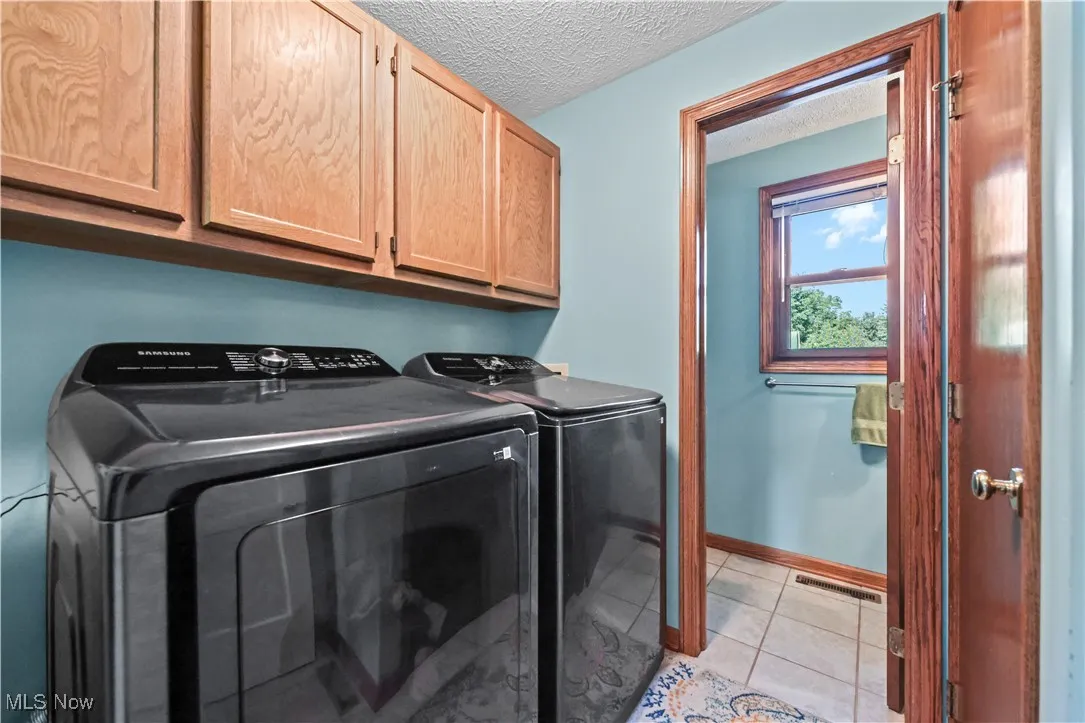 Washroom with cabinet space, independent washer and dryer, a textured ceiling, and light tile patterned floors