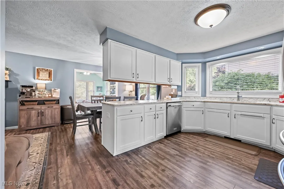 Kitchen with a textured ceiling, white cabinets, dark wood finished floors, dishwasher, and a peninsula