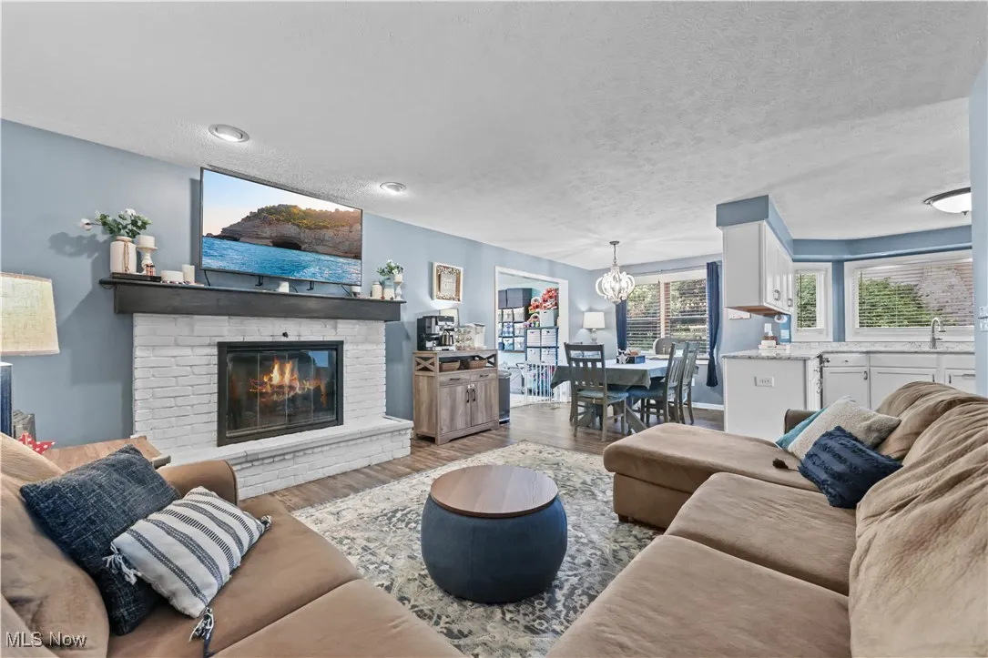 Living area with a chandelier, a textured ceiling, wood finished floors, and a brick fireplace