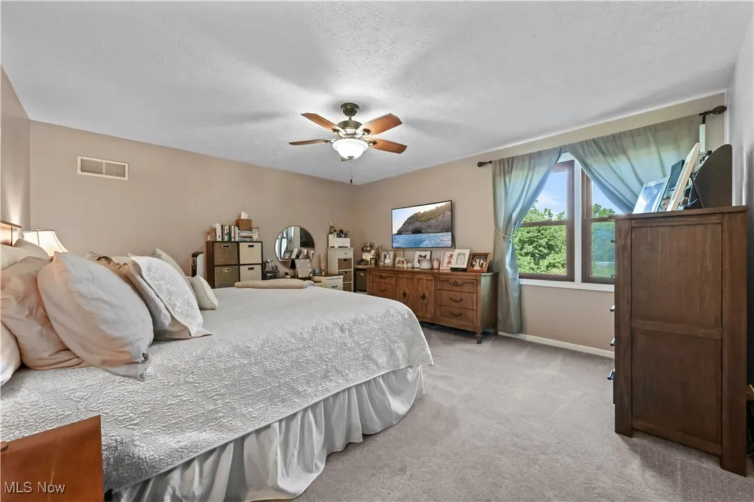 Bedroom with light carpet, ceiling fan, and a textured ceiling