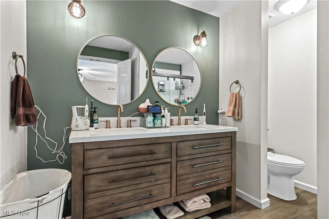 Bathroom featuring double vanity, tiled shower, and wood finished floors