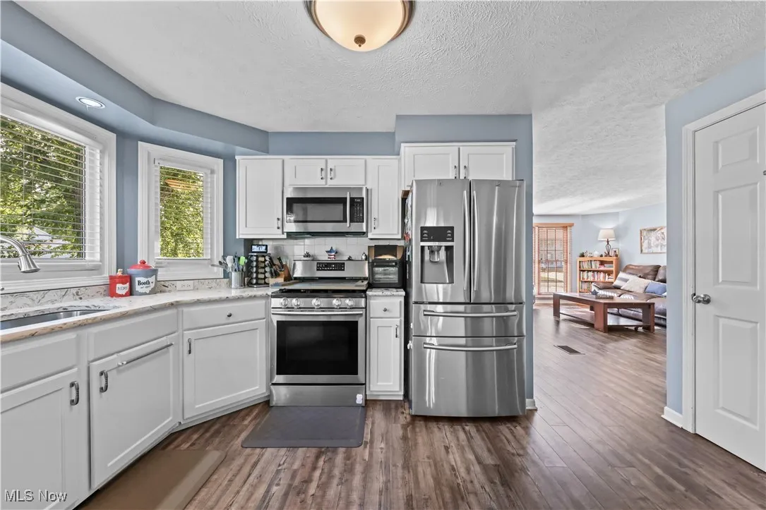 Kitchen with appliances with stainless steel finishes, dark wood-style flooring, a textured ceiling, white cabinets, and backsplash