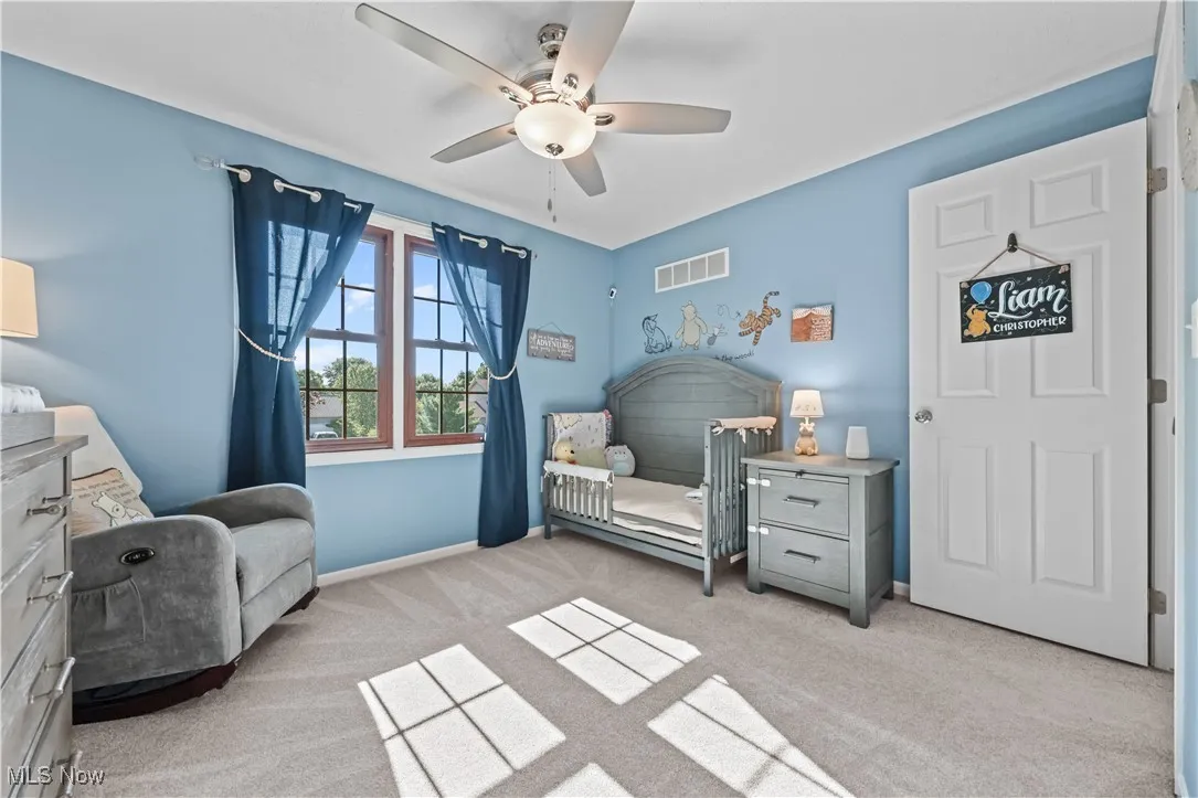 Bedroom featuring light colored carpet, a nursery area, and a ceiling fan