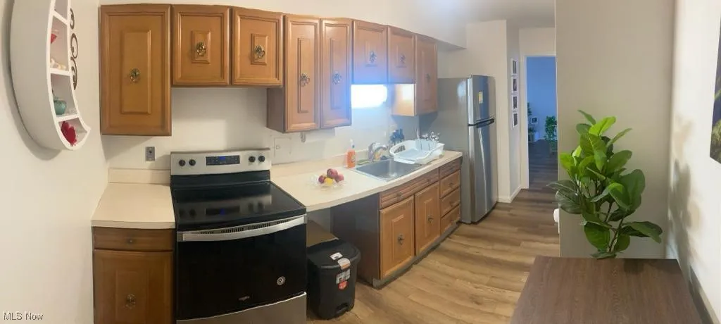 Kitchen featuring black range with electric stovetop, light countertops, light wood-style flooring, freestanding refrigerator, and brown cabinets