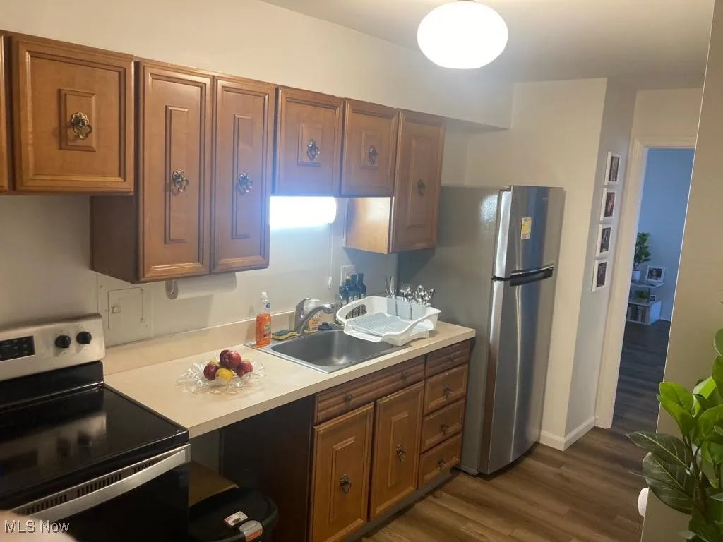 Kitchen featuring stainless steel appliances, light countertops, dark wood finished floors, and brown cabinetry