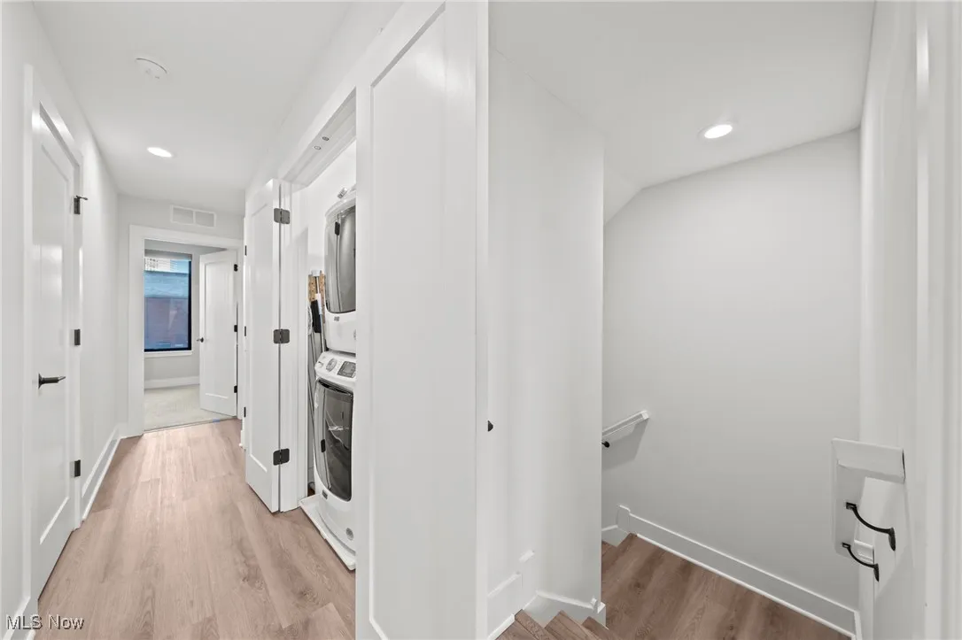 Laundry area with stacked washer / dryer, light wood-type flooring, and recessed lighting