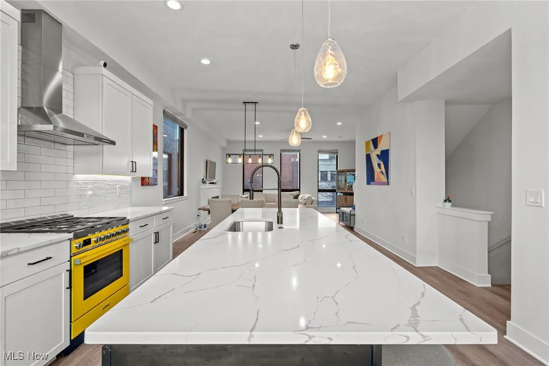 Kitchen featuring a large island with sink, wall chimney range hood, high end range, wood finished floors, and recessed lighting