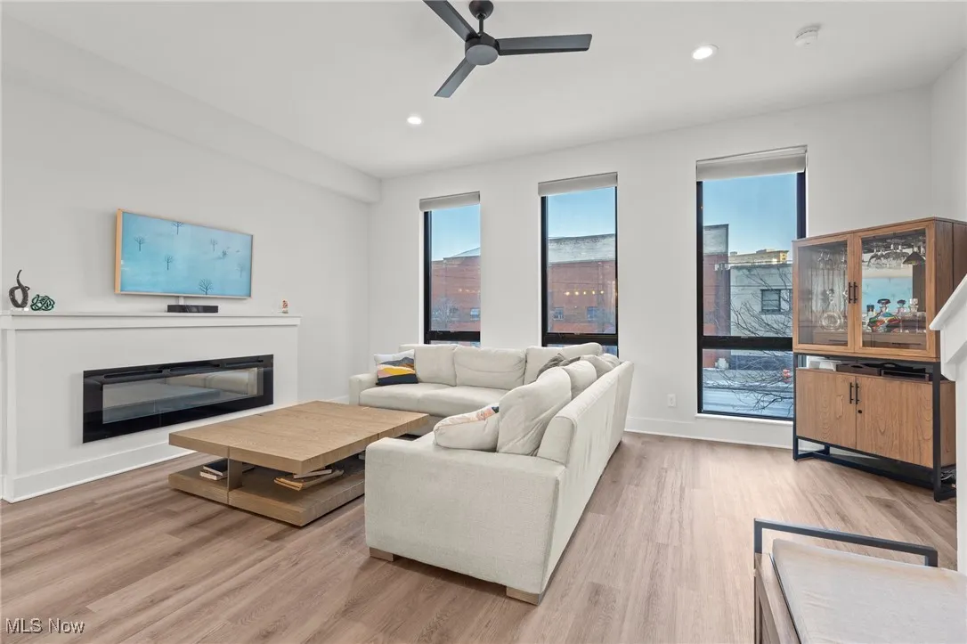 Living area with a ceiling fan, recessed lighting, light wood-style floors, and a glass covered fireplace