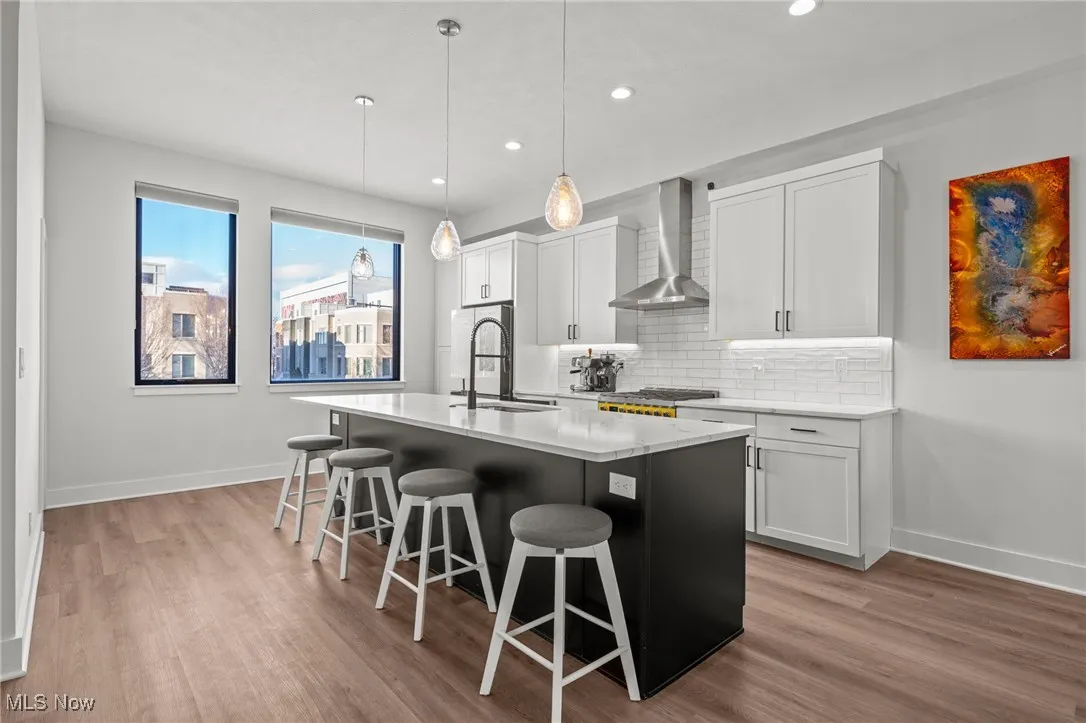 Kitchen featuring a center island with sink, wall chimney range hood, backsplash, a breakfast bar, and light wood-type flooring