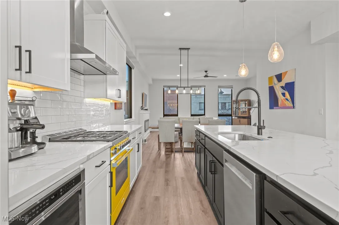 Kitchen featuring stainless steel appliances, wall chimney exhaust hood, white cabinets, recessed lighting, and light wood-style floors
