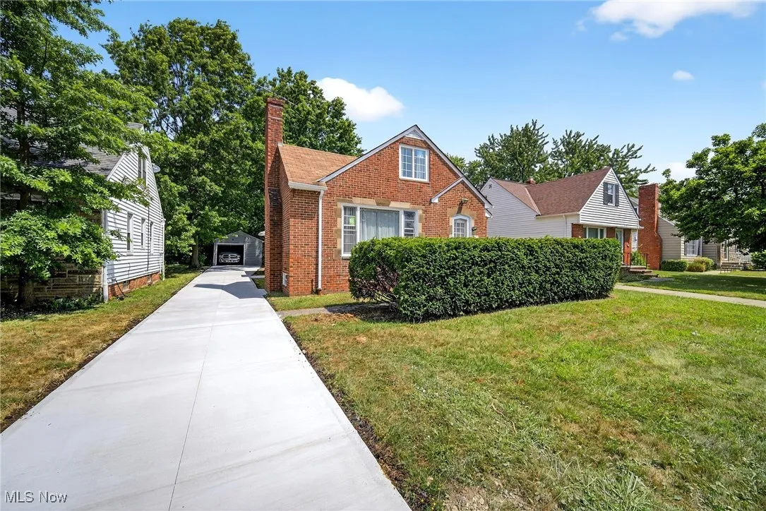 Bungalow-style home featuring a chimney, a front yard, brick siding, and a detached garage