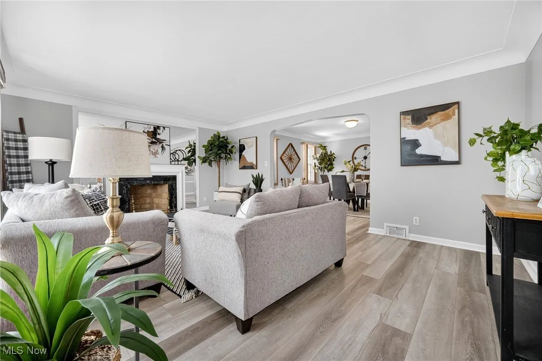 Living area with arched walkways, light wood finished floors, crown molding, and a premium fireplace