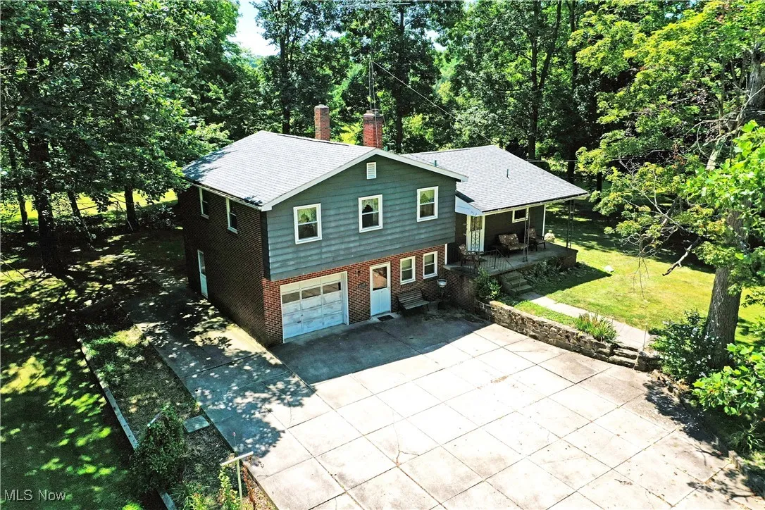 View of front facade featuring brick siding, concrete driveway, a chimney, an attached garage, and a porch