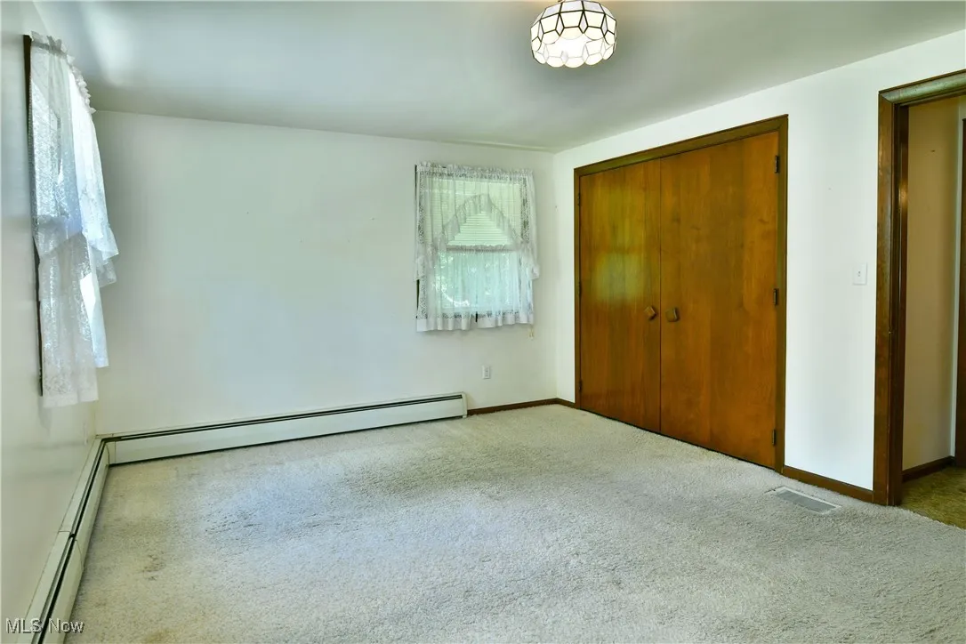 Unfurnished bedroom featuring carpet, a baseboard radiator, and a closet
