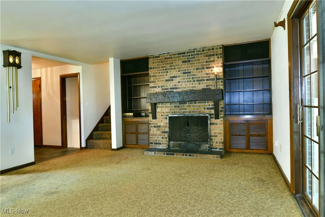 Unfurnished living room with carpet floors, stairway, a fireplace, and built in features