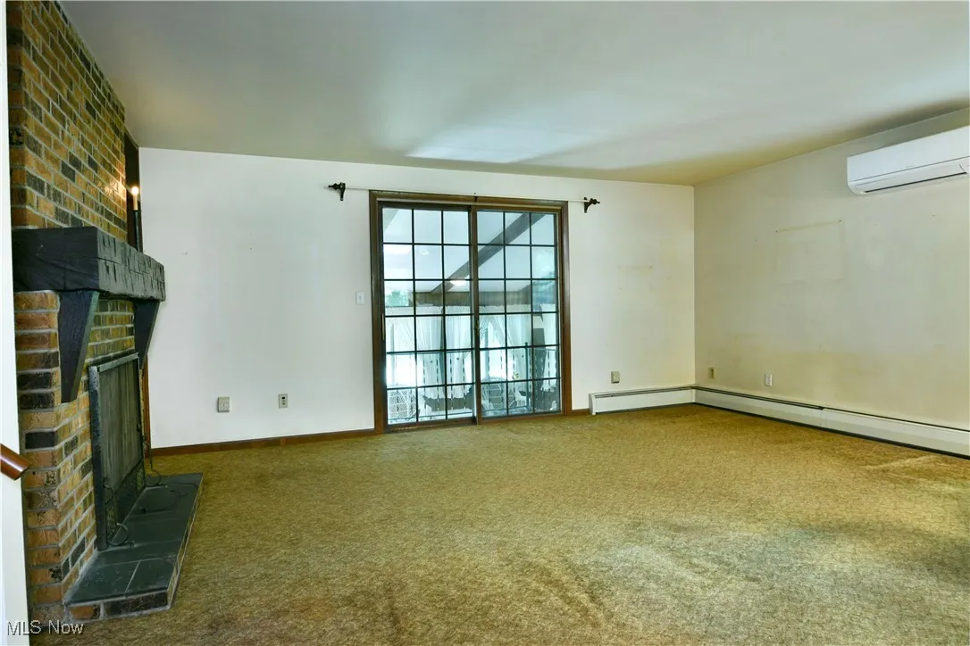 Unfurnished living room featuring a fireplace, carpet, and a wall mounted AC