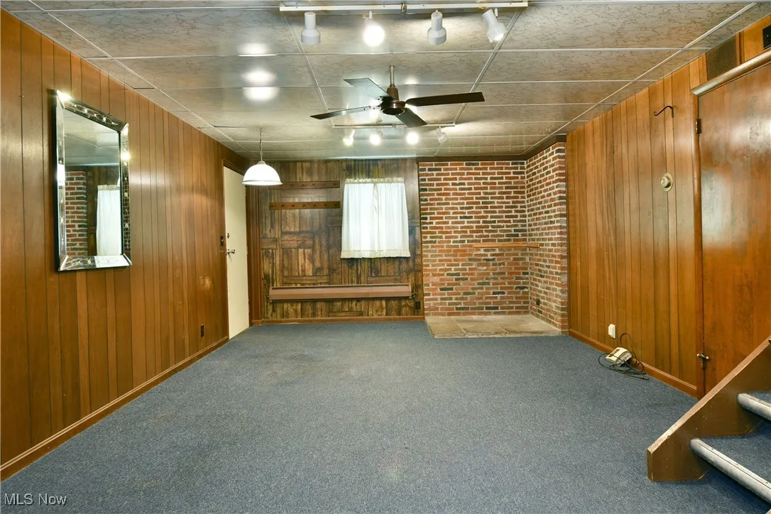 Unfurnished living room with wood walls, carpet flooring, a ceiling fan, and rail lighting
