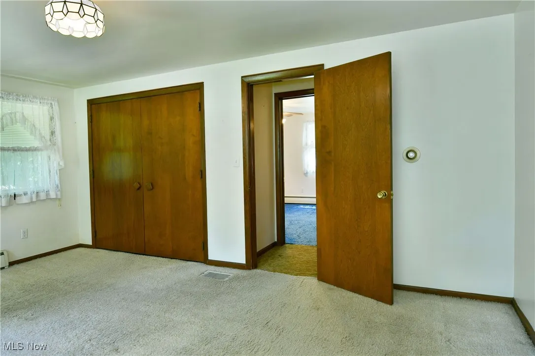 Unfurnished bedroom featuring carpet, a closet, and a baseboard heating unit