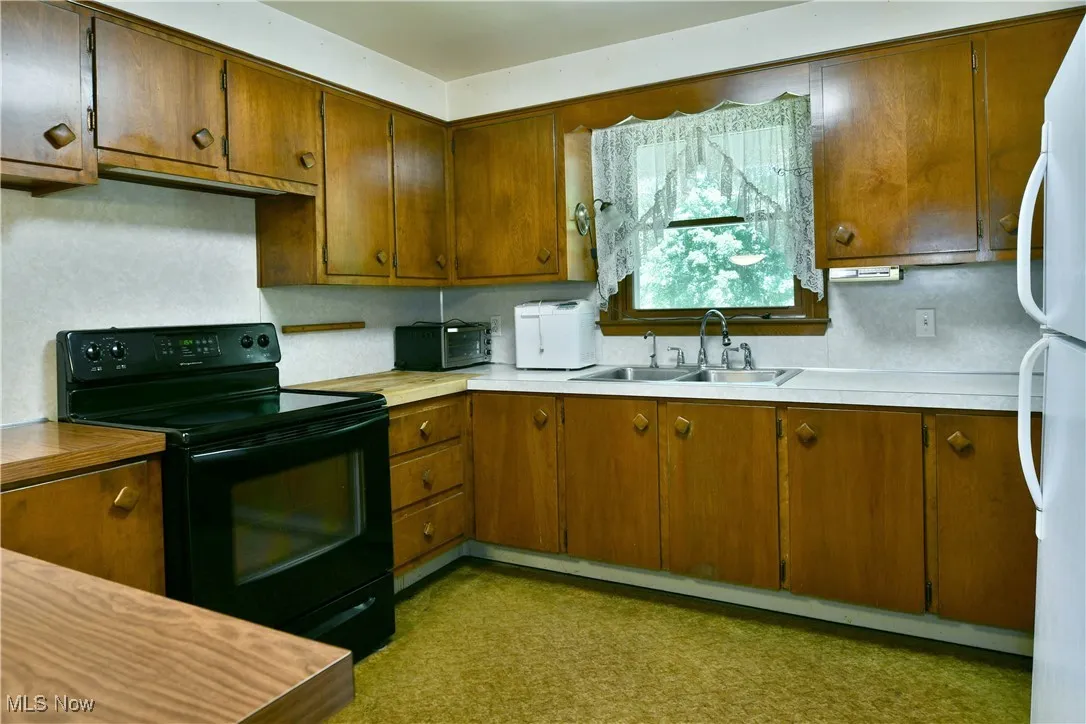 Kitchen featuring black / electric stove, freestanding refrigerator, light countertops, and brown cabinetry