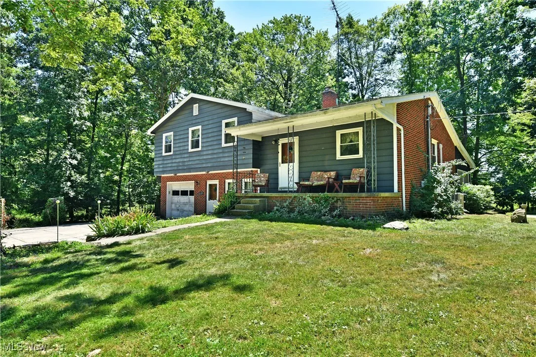 View of front of property featuring covered porch, a garage, brick siding, a chimney, and driveway