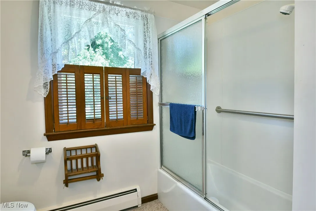 Full bathroom with a baseboard heating unit and bath / shower combo with glass door