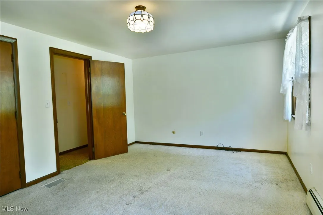 Unfurnished bedroom with carpet flooring and a baseboard radiator