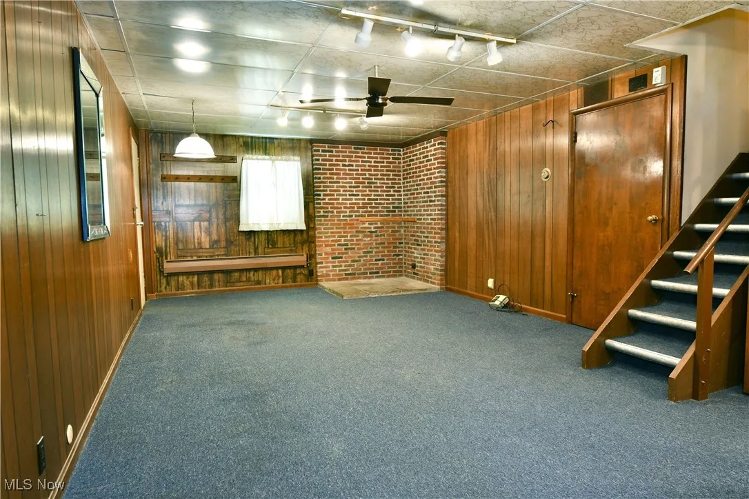 Basement featuring wood walls, carpet, a ceiling fan, rail lighting, and stairway