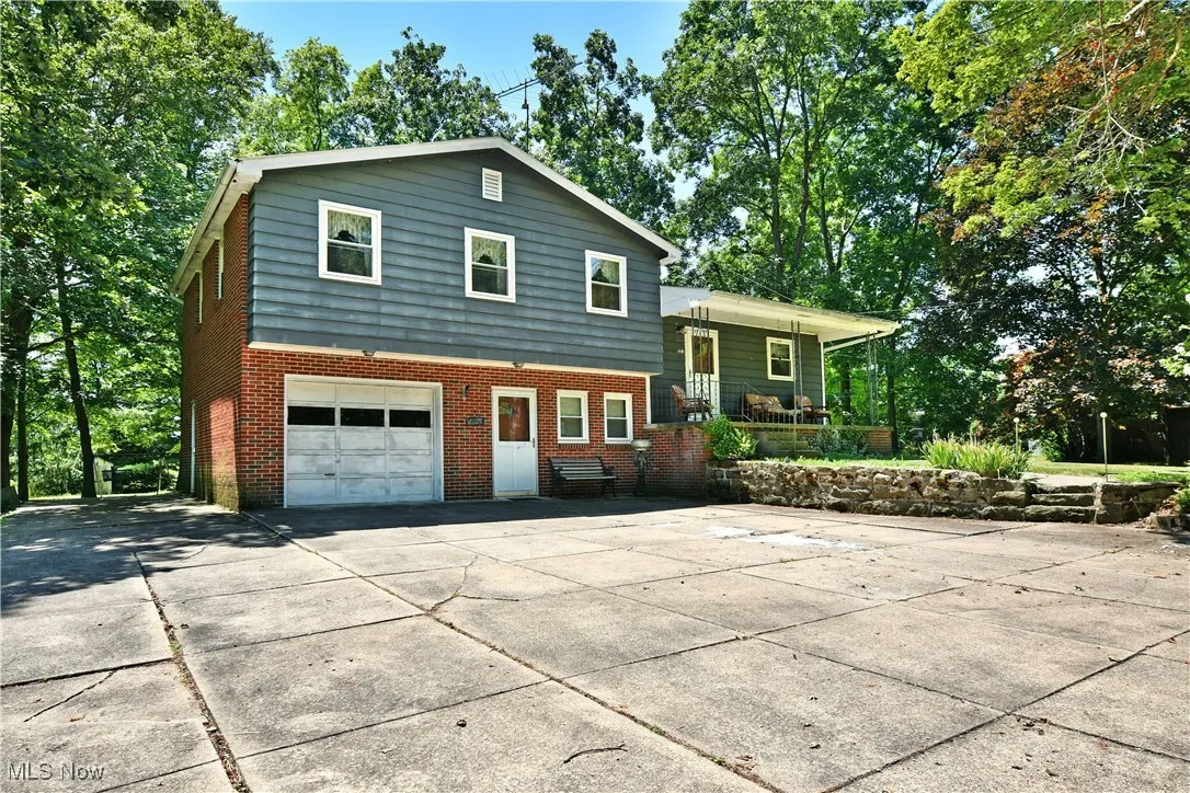Split level home featuring covered porch, brick siding, driveway, an attached garage, and view of scattered trees