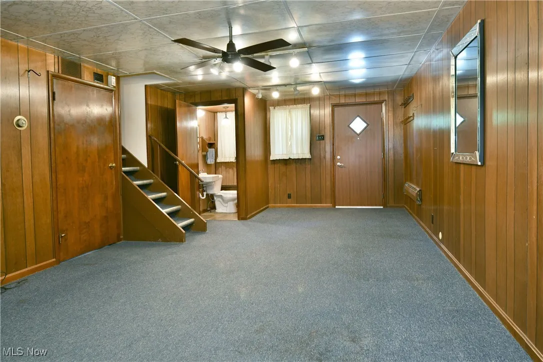 Foyer entrance featuring wood walls, carpet flooring, ceiling fan, and stairway