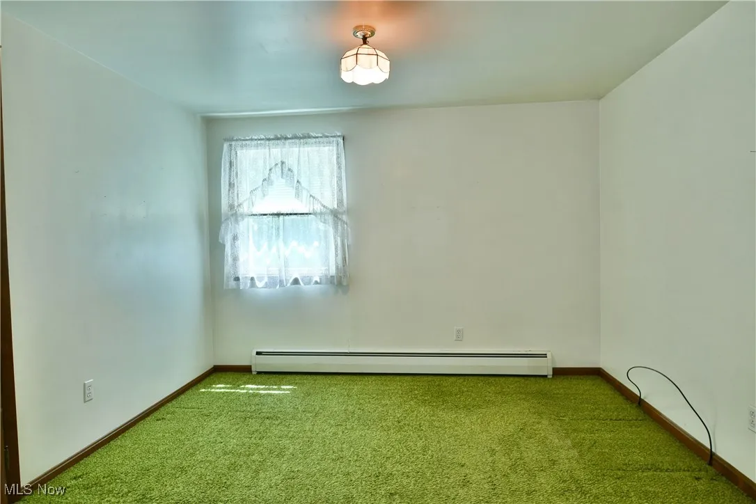 Carpeted empty room with baseboards and baseboard heating