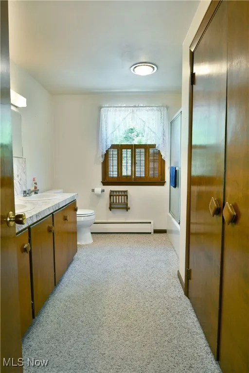 Bathroom featuring vanity, a baseboard heating unit, carpet, and bath / shower combo with glass door