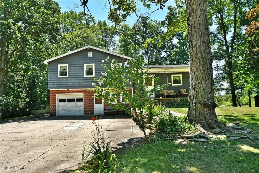 Split level home featuring an attached garage, brick siding, driveway, and a front yard