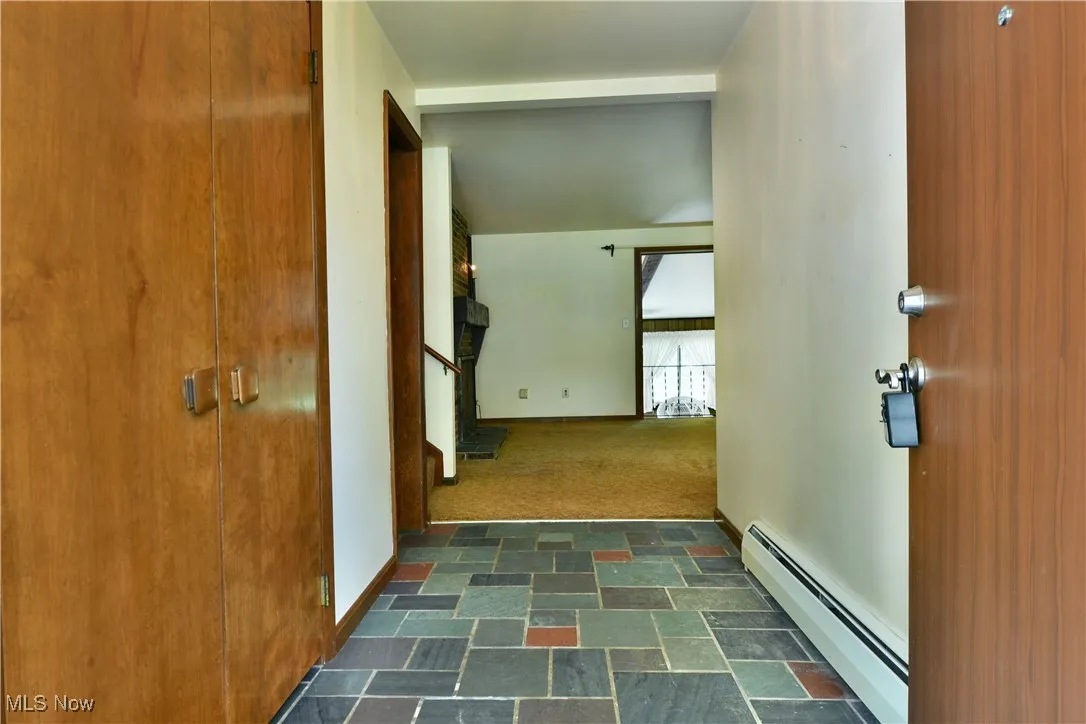 Corridor with baseboard heating, stairs, dark stone finish floors, and dark carpet