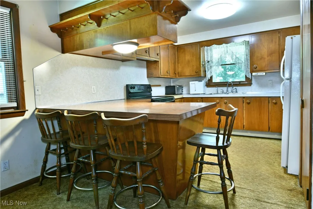 Kitchen featuring brown cabinets, a peninsula, freestanding refrigerator, and black electric range