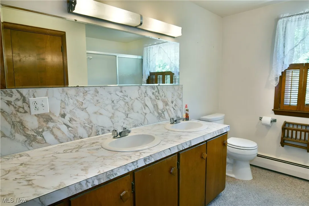 Bathroom with tasteful backsplash, double vanity, a shower with door, and a baseboard heating unit