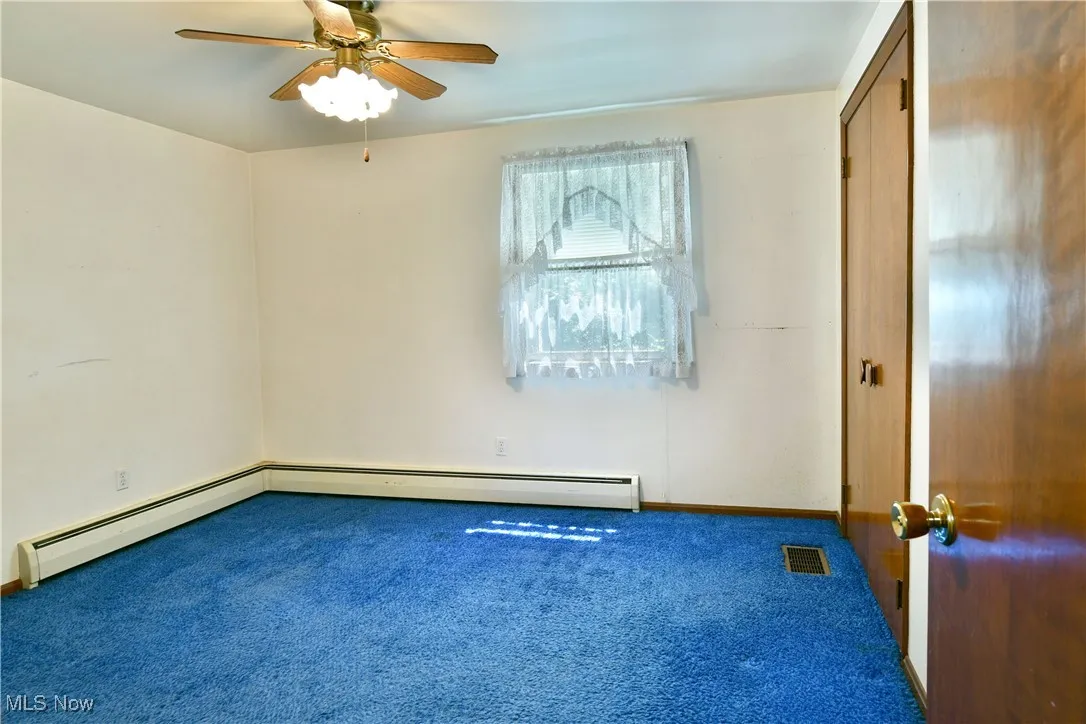 Unfurnished bedroom featuring carpet flooring, a baseboard heating unit, and a ceiling fan