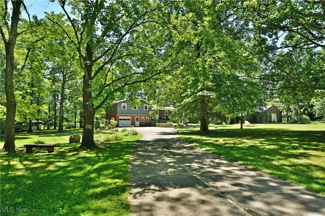 Tri-level home featuring driveway, a garage, a front lawn, and view of scattered trees