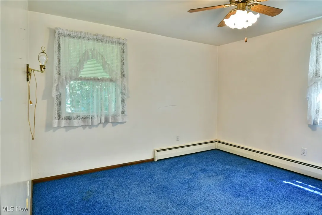 Carpeted empty room featuring a ceiling fan and a baseboard heating unit