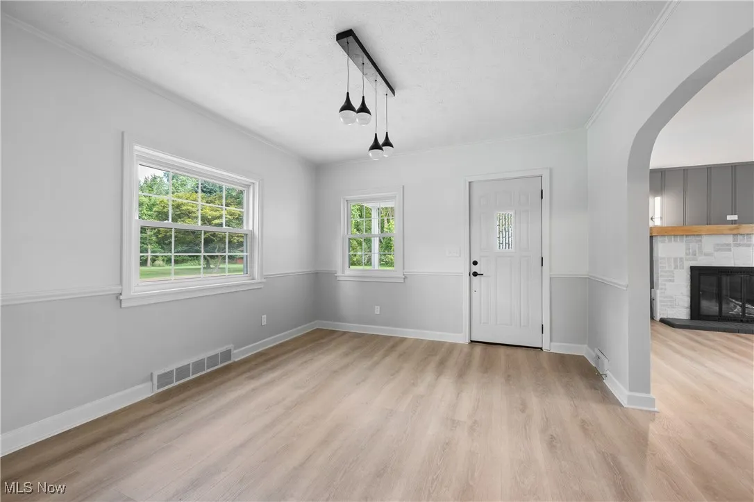 Entrance foyer with ornamental molding, a textured ceiling, light wood-style floors, arched walkways, and a fireplace