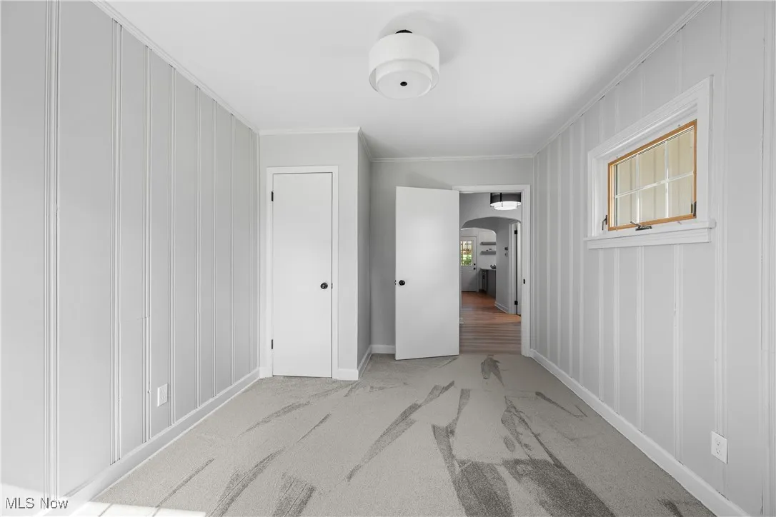 Unfurnished bedroom featuring arched walkways, carpet floors, and ornamental molding