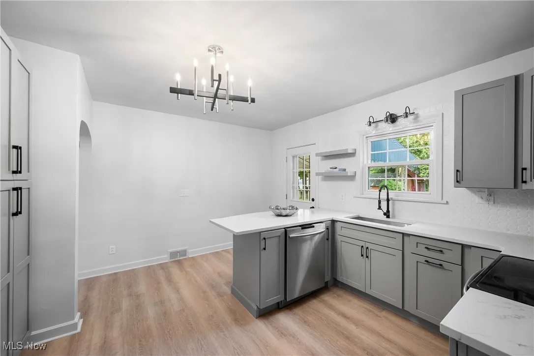 Kitchen featuring gray cabinetry, a peninsula, stainless steel dishwasher, a chandelier, and light wood finished floors