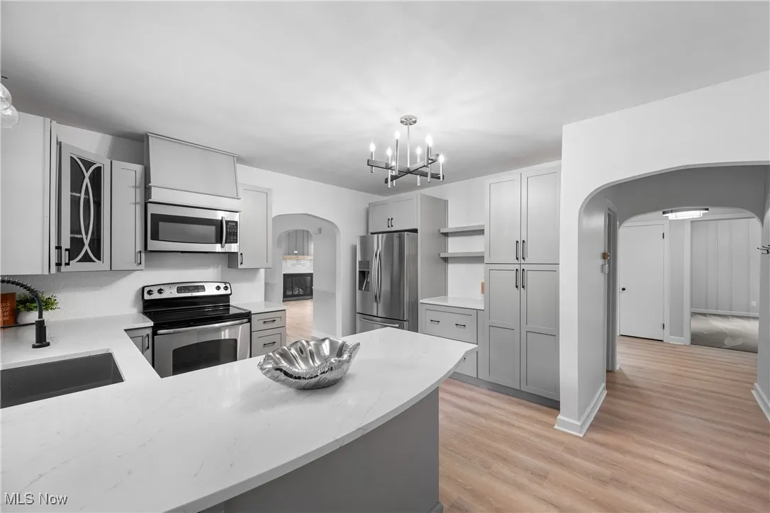 Kitchen featuring arched walkways, appliances with stainless steel finishes, light wood-style floors, and a chandelier