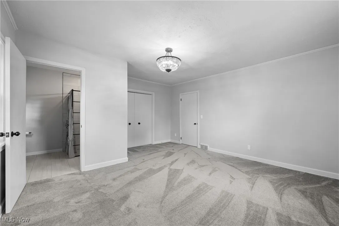 Unfurnished bedroom with carpet, crown molding, and a chandelier