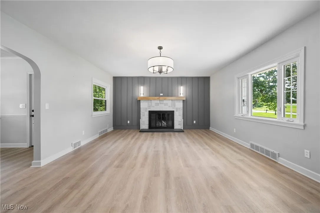 Unfurnished living room with light wood finished floors, arched walkways, a stone fireplace, and a chandelier